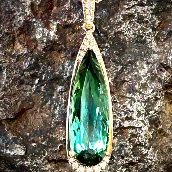 Diamond Accented Elongated Pear Shape Green Tourmaline Pendant In Warm Yellow Gold.