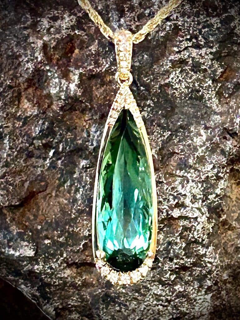 Diamond Accented Elongated Pear Shape Green Tourmaline Pendant In Warm Yellow Gold.